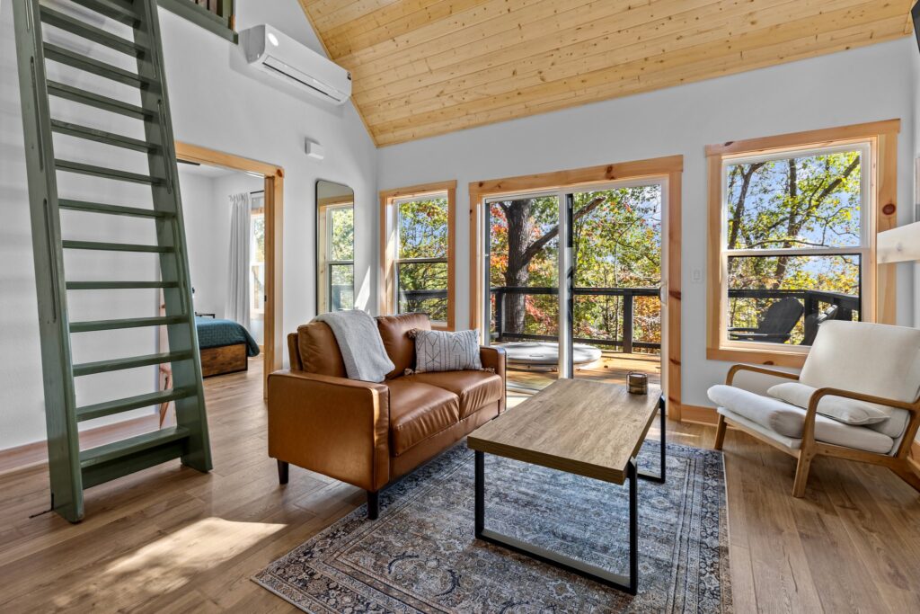 Bright living area with loft ladder and large windows overlooking the woods